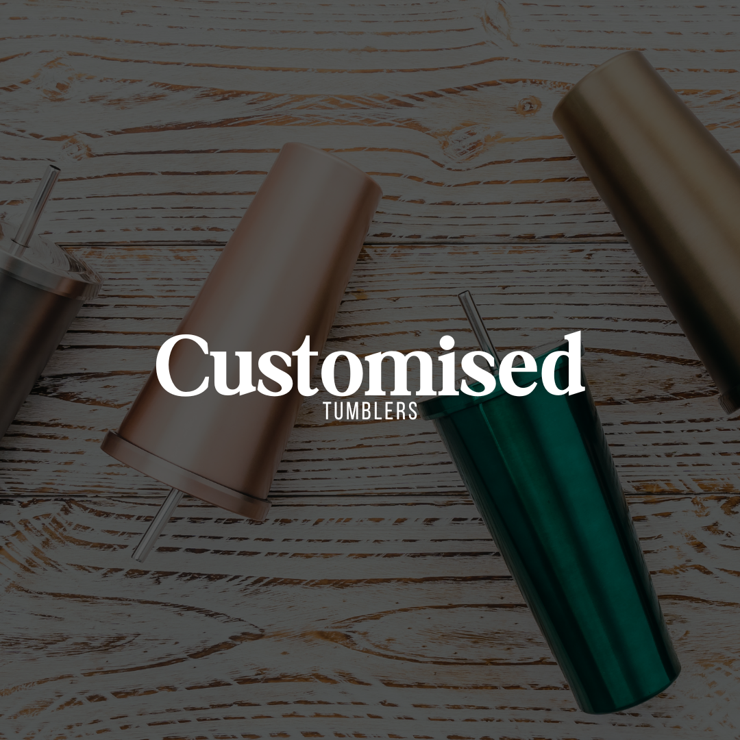 Flat lay of sleek metal tumblers in various colors with straws, arranged on a rustic wooden background. Text overlay reads "Customised Tumblers"