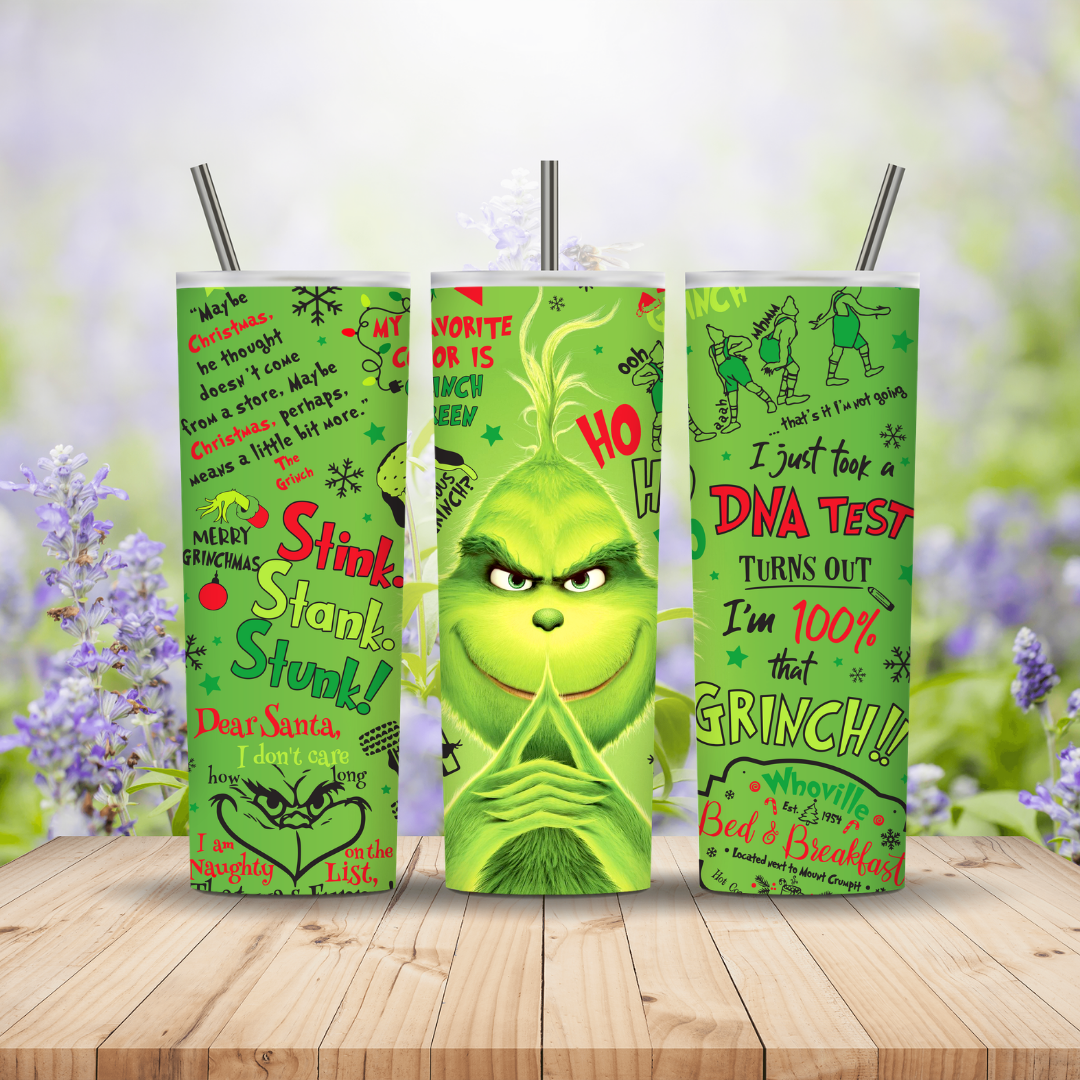 Three green tumblers with Grinch-themed designs on a wooden surface with a blurred floral background.