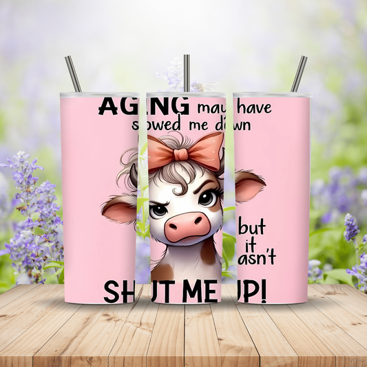 Three pink tumblers with a cow design and text on a wooden surface with a blurred floral background.