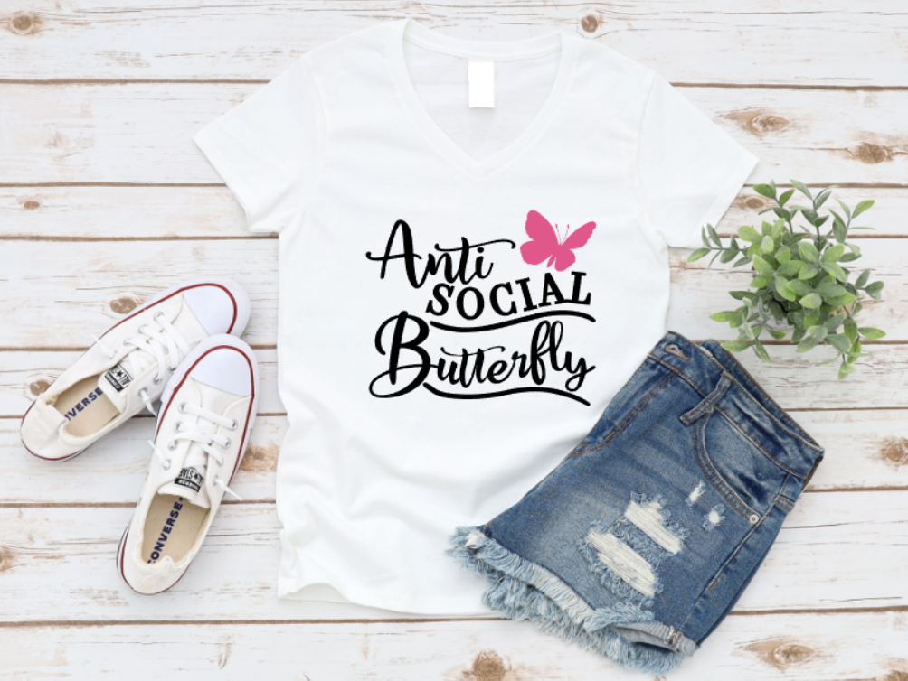 White V-neck t-shirt with “Anti Social Butterfly” text and a pink butterfly graphic, styled alongside distressed denim shorts, white Converse sneakers, and a potted plant on a whitewashed wooden backdrop.