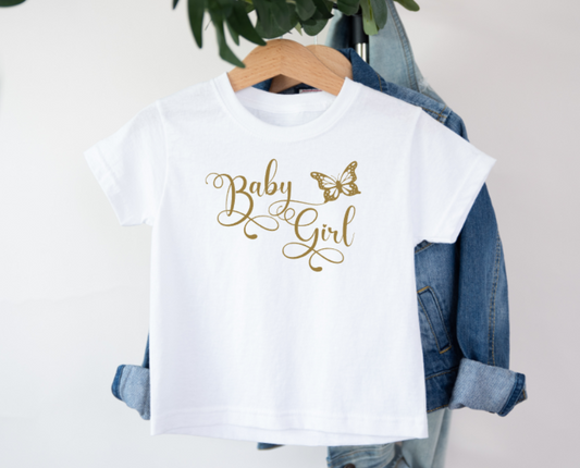 White t-shirt with 'Baby Girl' text and butterfly graphic on a hanger with denim jacket.
