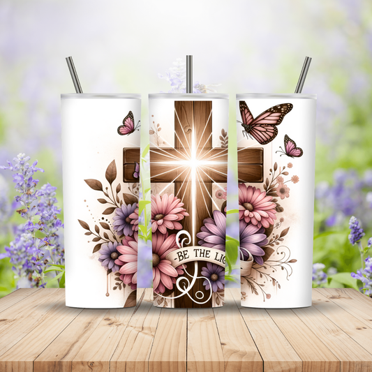 Three tumblers with cross and floral designs on a wooden surface with blurred flowers in the background