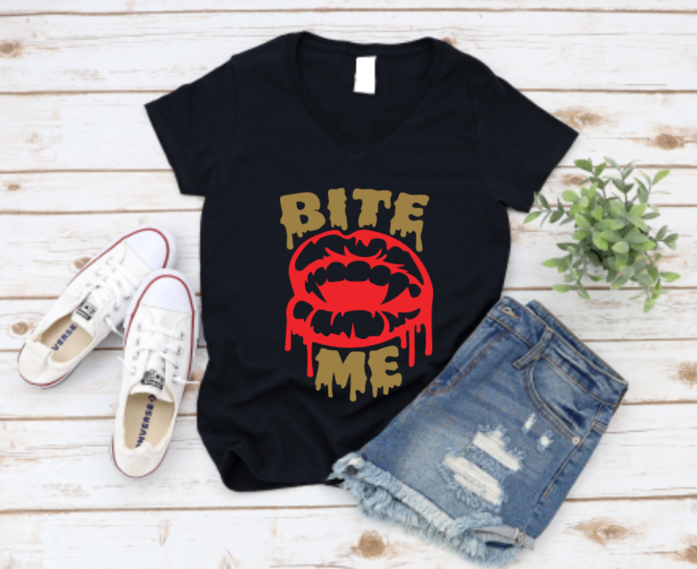 Black t-shirt with bold red vampire lips and dripping "Bite Me" text, styled with white sneakers and ripped denim shorts on a light wooden background.