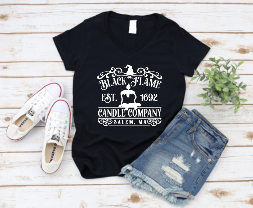 Black t-shirt with “Black Flame Candle Company – Salem, MA” graphic, styled with denim shorts and white sneakers on a rustic wooden background.