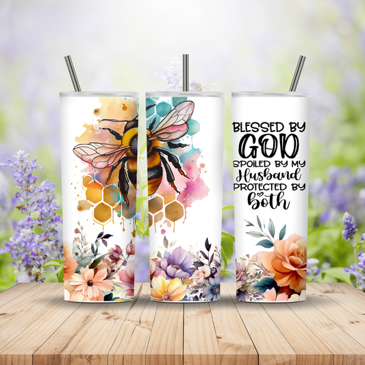 Three tumblers with floral and bee designs on a wooden surface with a blurred nature background.