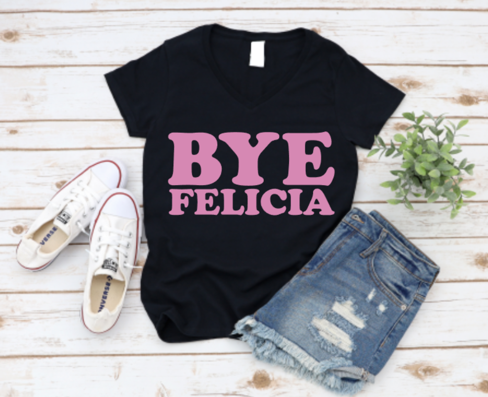 Black t-shirt with bold pink “Bye Felicia” text, styled with denim shorts, sneakers, and a green plant on a wooden background.