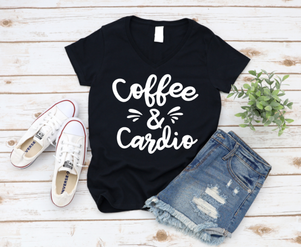 Black t-shirt with “Coffee & Cardio” text in white, styled with ripped denim shorts and white sneakers on a wooden surface.