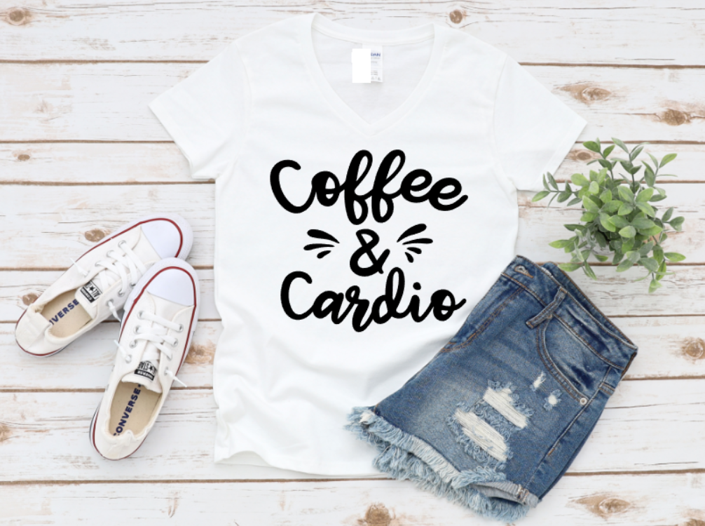 White t-shirt with “Coffee & Cardio” text in white, styled with ripped denim shorts and white sneakers on a wooden surface.