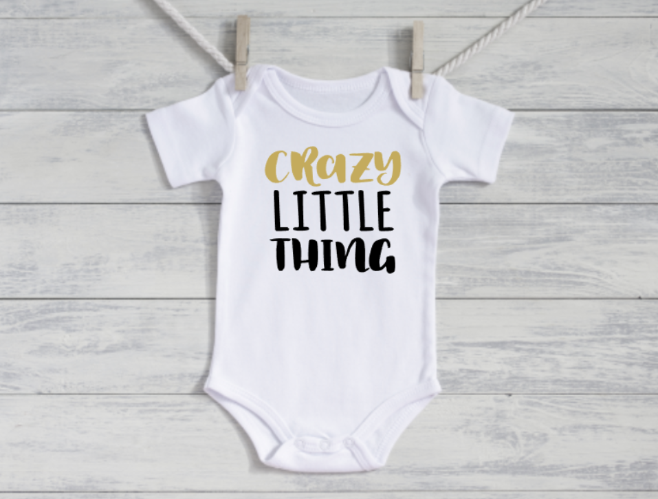 White baby onesie with 'Crazy Little Thing' text on a wooden surface