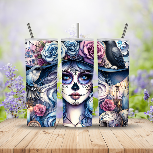 Decorative Tumblers with a colourful design of a woman's face, flowers, and a raven on a wooden surface with a blurred floral background.