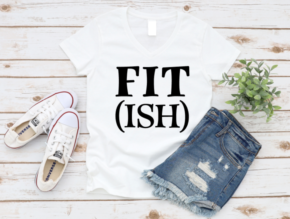 White t-shirt with 'FIT (ISH)' text, denim shorts, and white sneakers on a wooden surface.