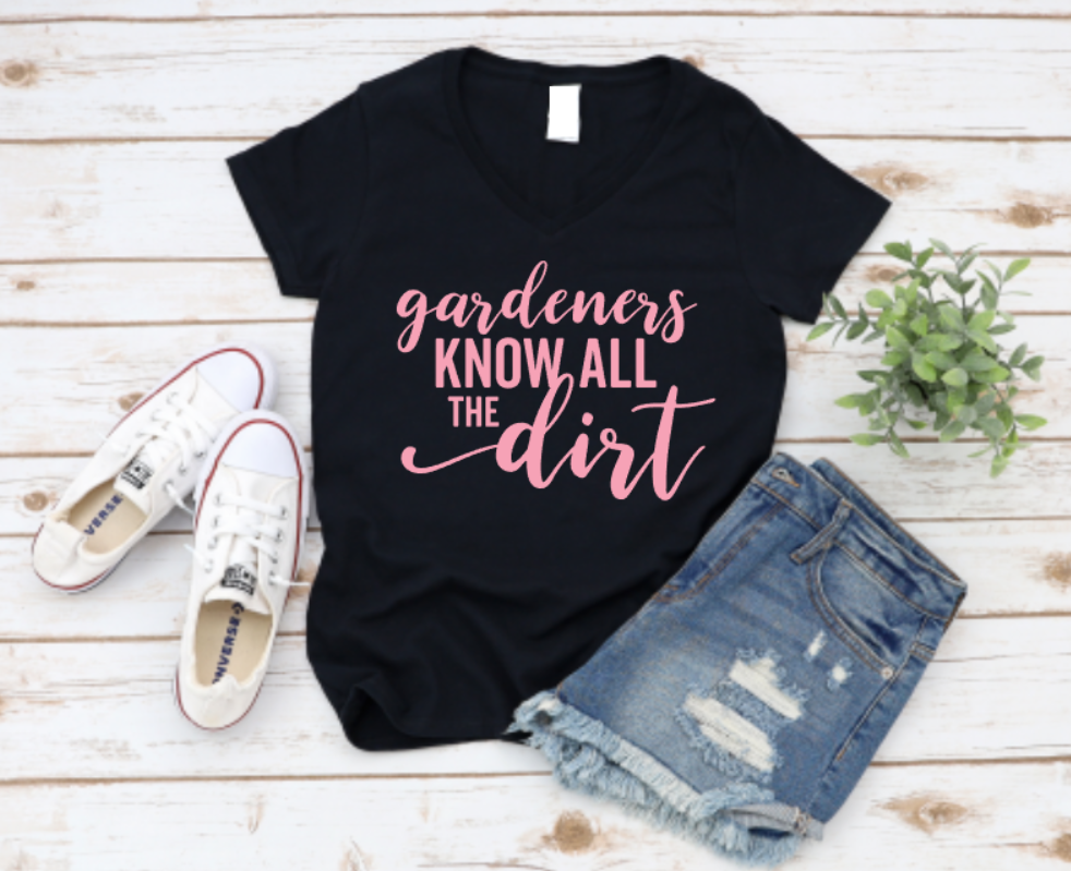 Black t-shirt with 'gardeners know all the dirt' text, paired with jeans and sneakers on a wooden surface.