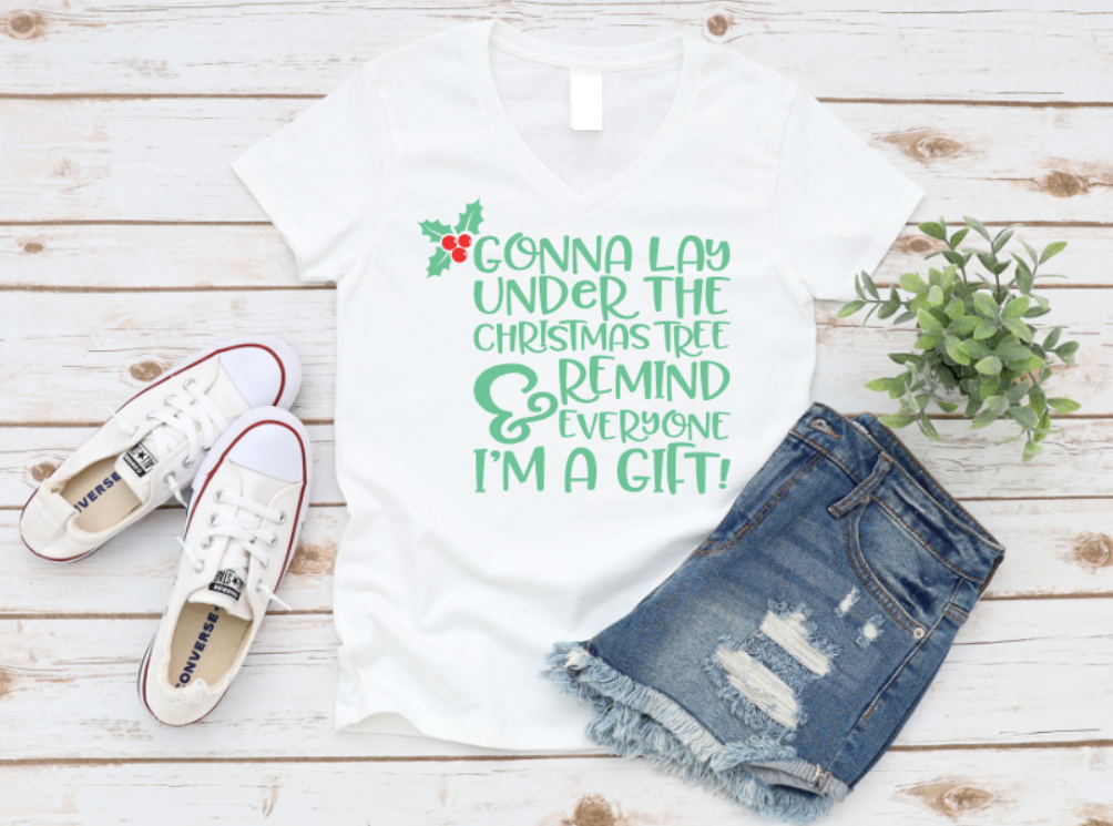 White t-shirt with Christmas-themed text, denim shorts, and sneakers on a wooden surface.