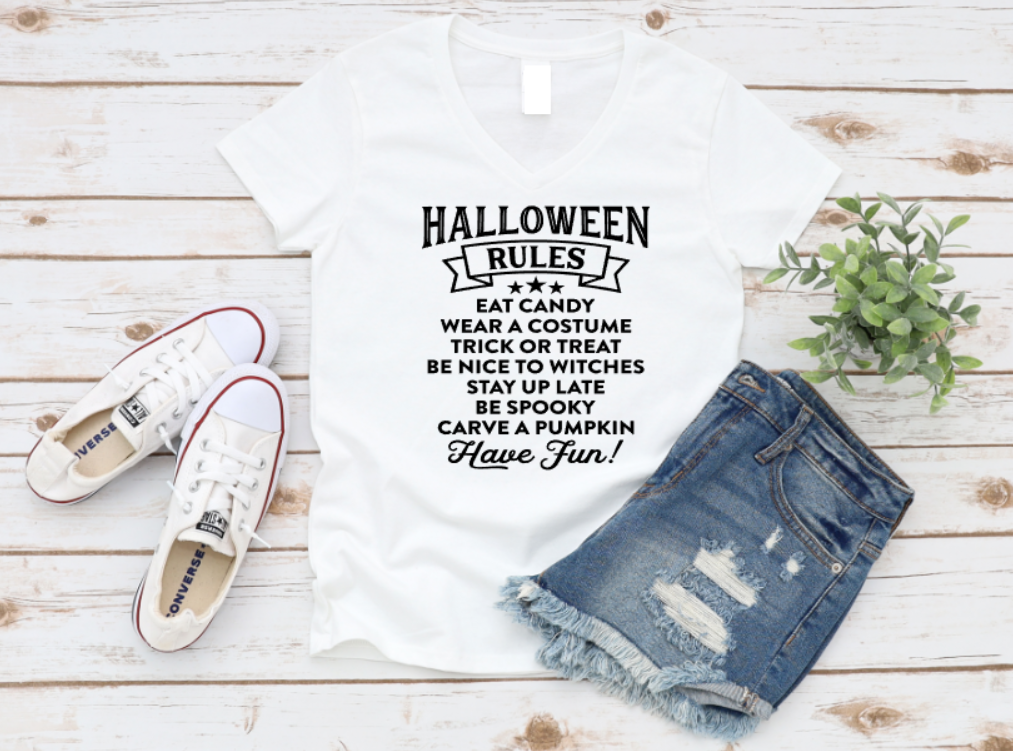 White t-shirt with Halloween rules text, denim shorts, and white sneakers on a wooden surface.
