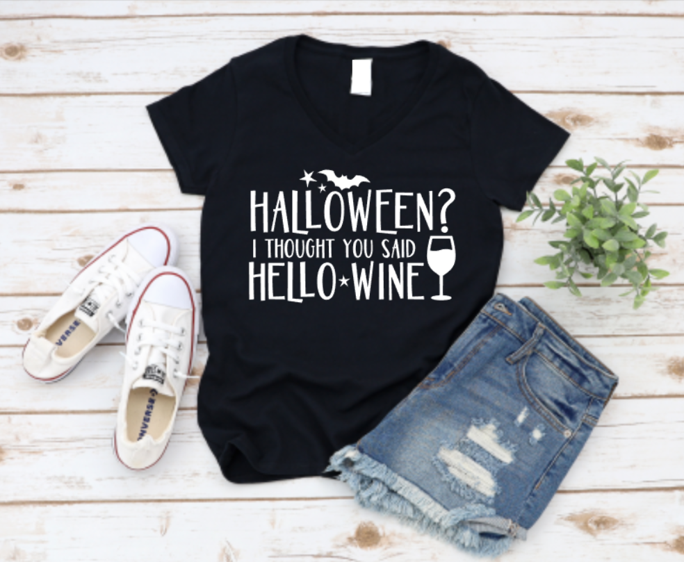 Black t-shirt with 'Halloween? I thought you said hello wine' text, paired with denim shorts and white sneakers on a wooden surface.