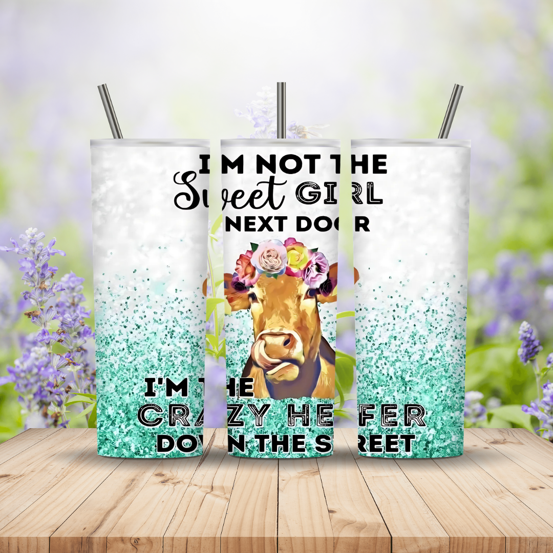 Three tumblers with a cow design and text on a wooden surface with a floral background