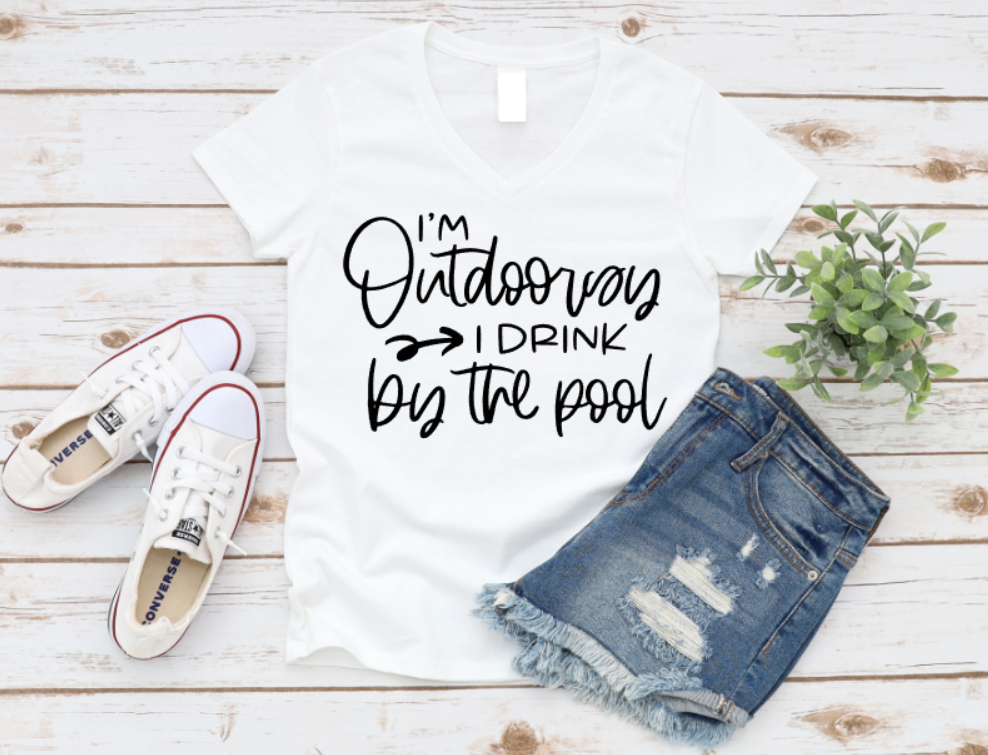 White t-shirt with 'I'm Outdoorsy I Drink by the Pool' text, paired with denim shorts and white sneakers on a wooden surface. www.missmafia.com