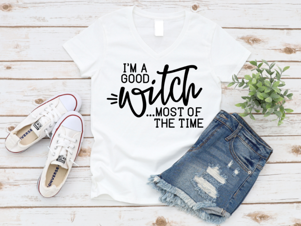White t-shirt with 'I'm a good witch most of the time' text, paired with denim shorts and sneakers on a wooden surface. Shop now at www.missmafia.com