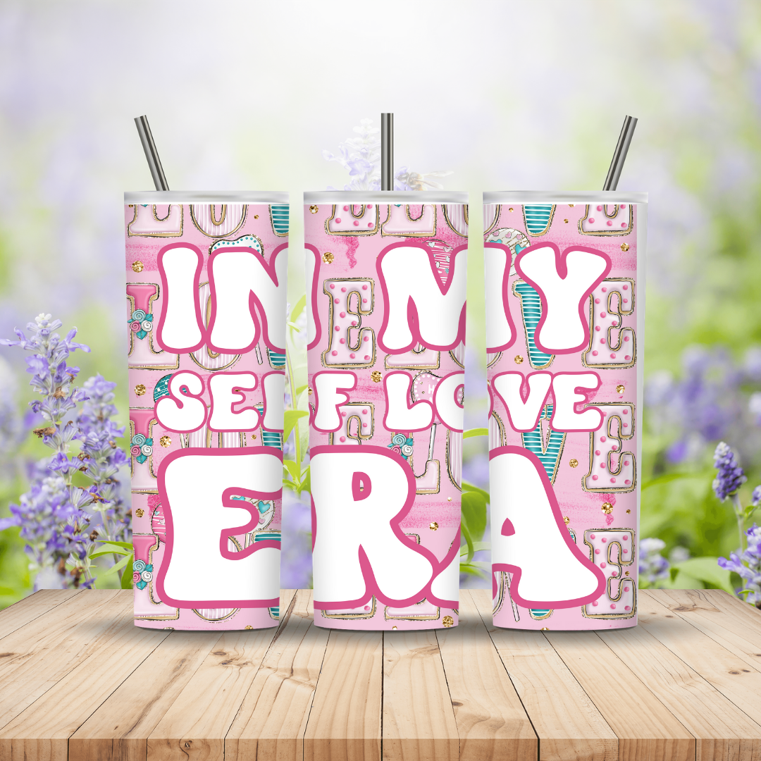 Three pink tumblers with decorative text on a wooden surface with a blurred floral background