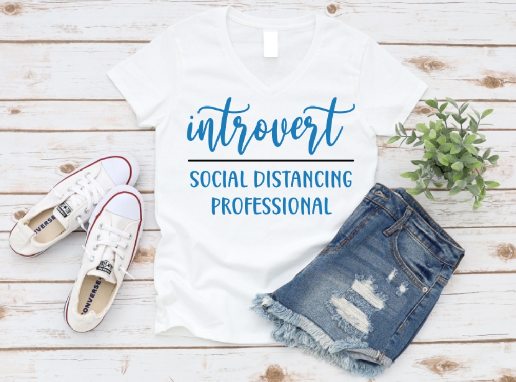 T-shirt with 'introvert social distancing professional' text, paired with jeans and sneakers on a wooden surface. www.missmafia.com
