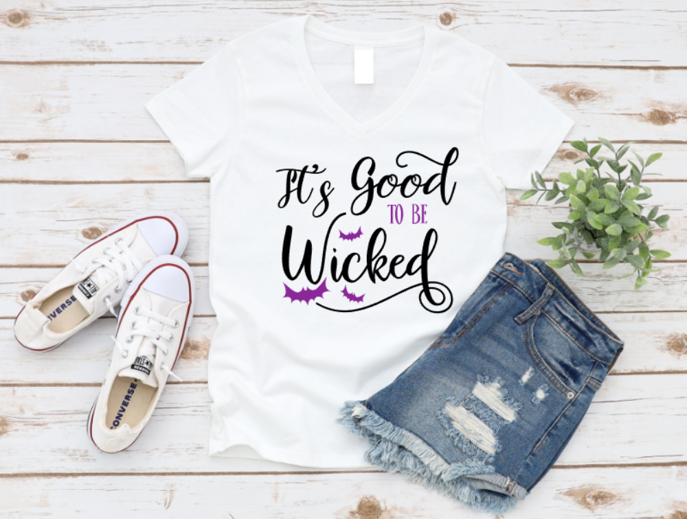 White t-shirt with 'It's Good to be Wicked' text, white sneakers, and denim shorts on a wooden surface. www.missmafia.com