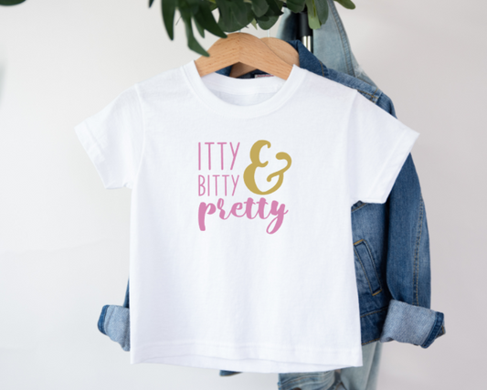 White t-shirt with 'Itty Bitty & Pretty' text on a hanger with denim jacket.