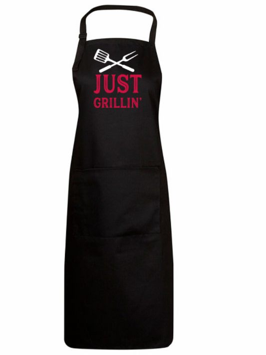 Black apron with 'JUST GRILLIN'' text and grill tools graphic on a white background