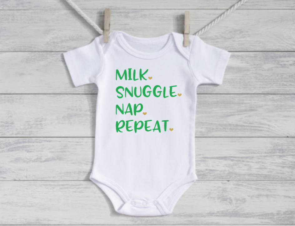 White baby onesie with green text on a wooden background