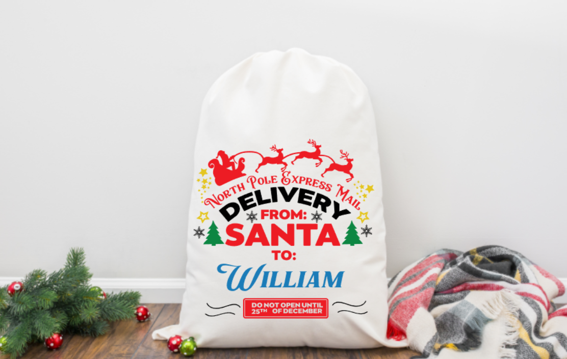 White Santa sack with festive text and graphics on a wooden floor with Christmas decorations.