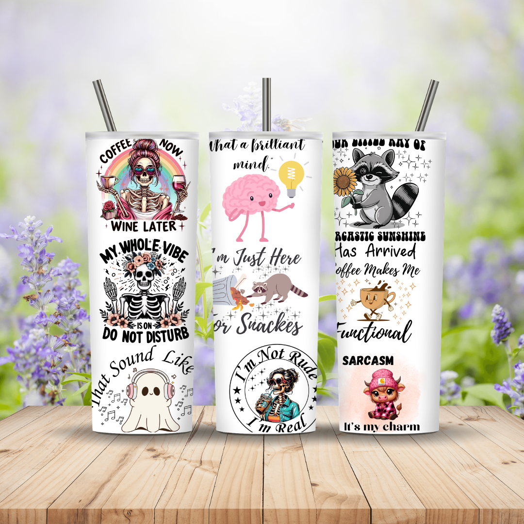 Three tumblers with various designs and text on a wooden surface with a blurred floral background.