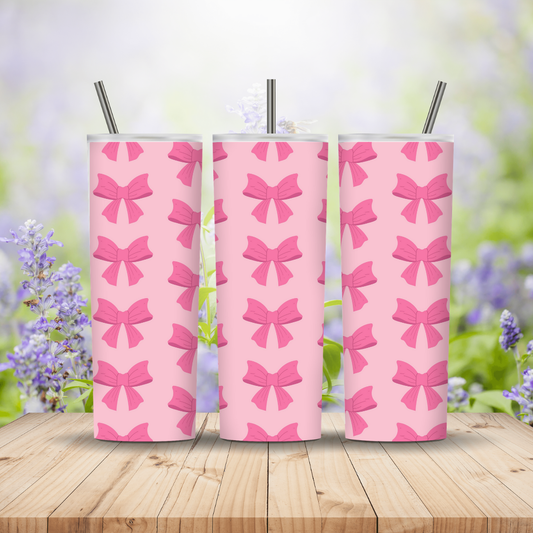Three pink tumblers with bow pattern on a wooden surface with a blurred floral background