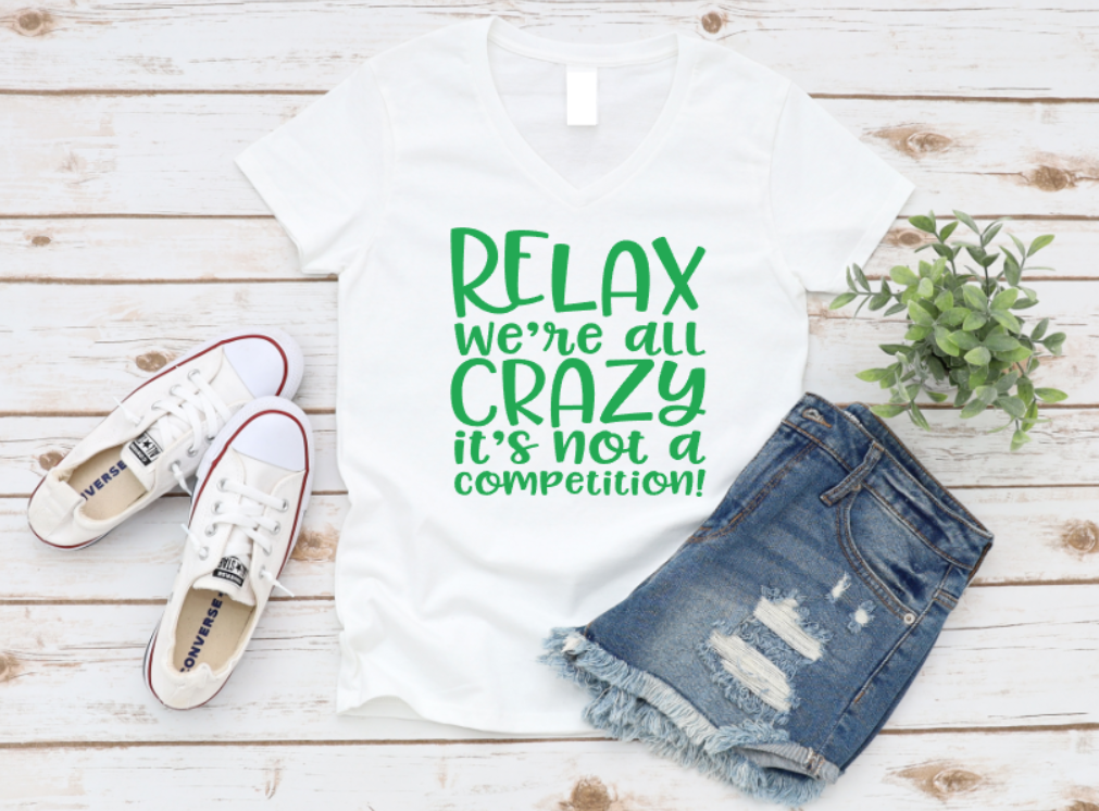 T-shirt with 'Relax, we're all crazy, it's not a competition!' text, paired with denim shorts and white sneakers on a wooden surface. www.missmafia.com