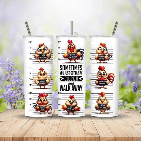 Three tumblers with cartoon rooster designs and humorous text on a wooden surface with a blurred floral background.