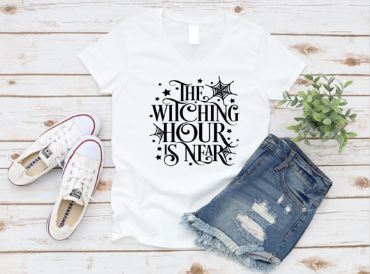White t-shirt with 'The Witching Hour is Near' text, denim shorts, and white sneakers on a wooden surface. www.missmafia.com