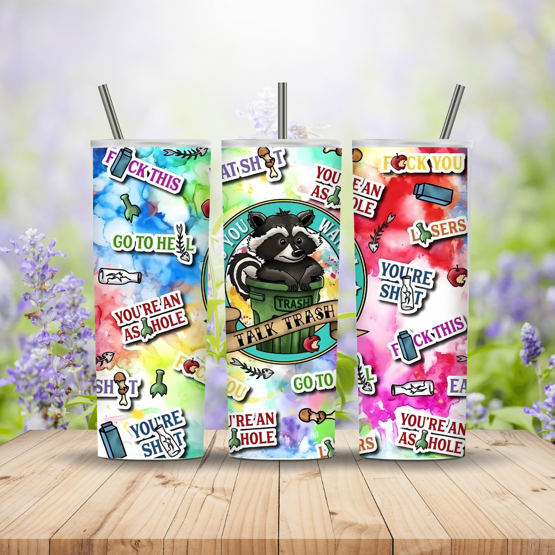 Three colorful drink containers with graphic designs and text on a wooden surface with a blurred floral background.