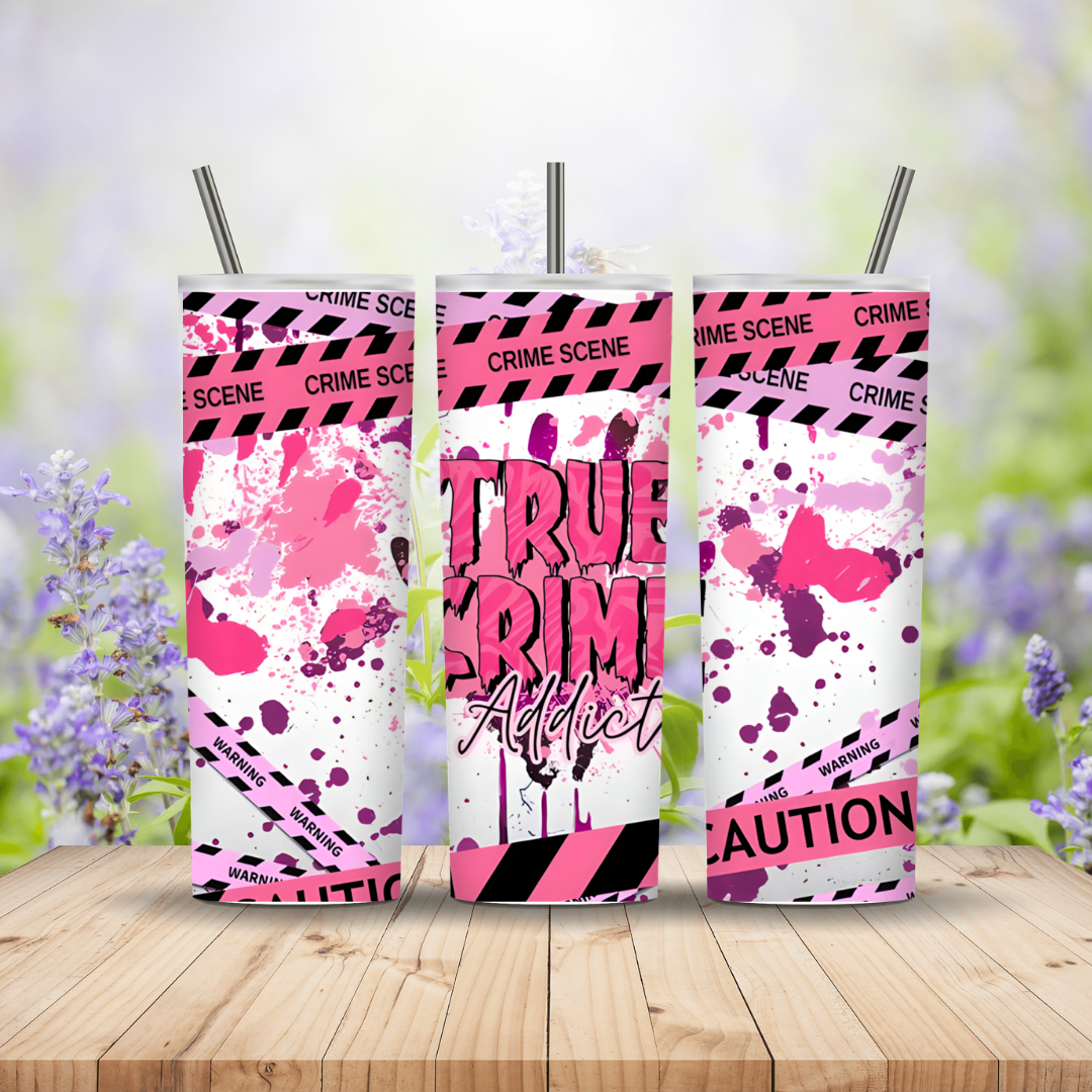 Three pink and black tumblers with 'True Crime Addict' text on a wooden surface with a blurred floral background.