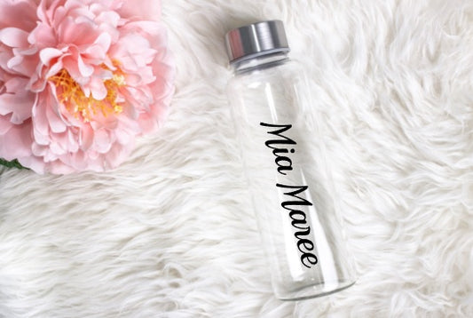 Clear water bottle with 'Mia Maree' branding on a white fluffy surface with a pink flower.