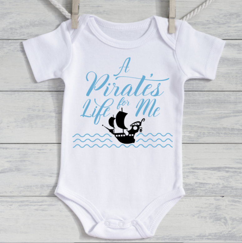 White baby onesie with blue text and ship graphic on a wooden surface