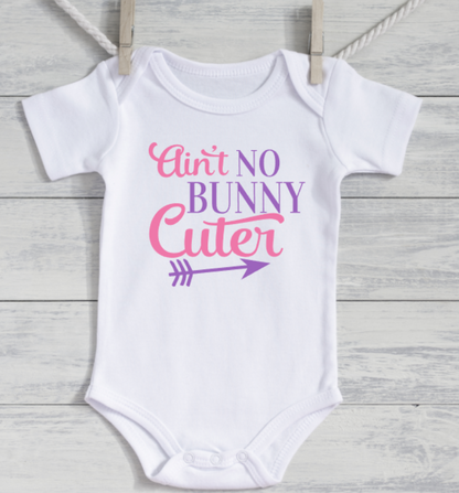 White baby onesie with pink and purple text on a wooden surface