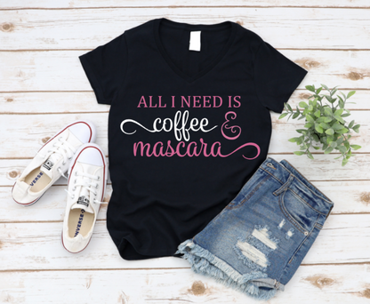 Black V-neck t-shirt with the phrase "All I Need Is Coffee & Mascara" in white and pink text, styled with white Converse sneakers, ripped denim shorts, and a green plant on a white wooden background.