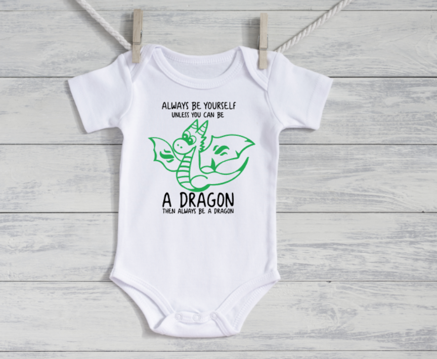 White baby onesie with a dragon graphic and text on a wooden surface