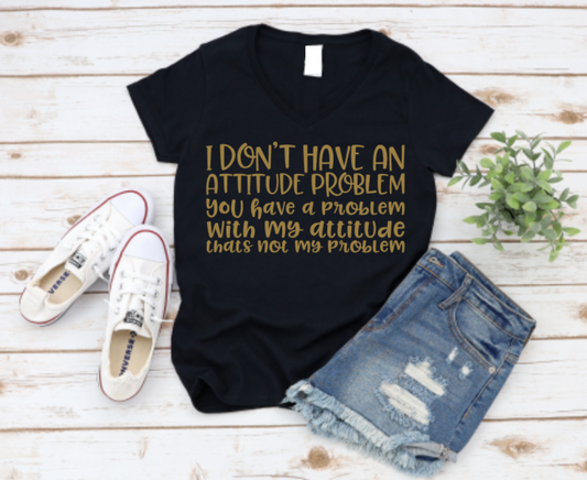 Black V-neck t-shirt with gold text that reads “I don’t have an attitude problem. You have a problem with my attitude—that’s not my problem,” styled with ripped denim shorts, white Converse sneakers, and a small plant on a wooden background.