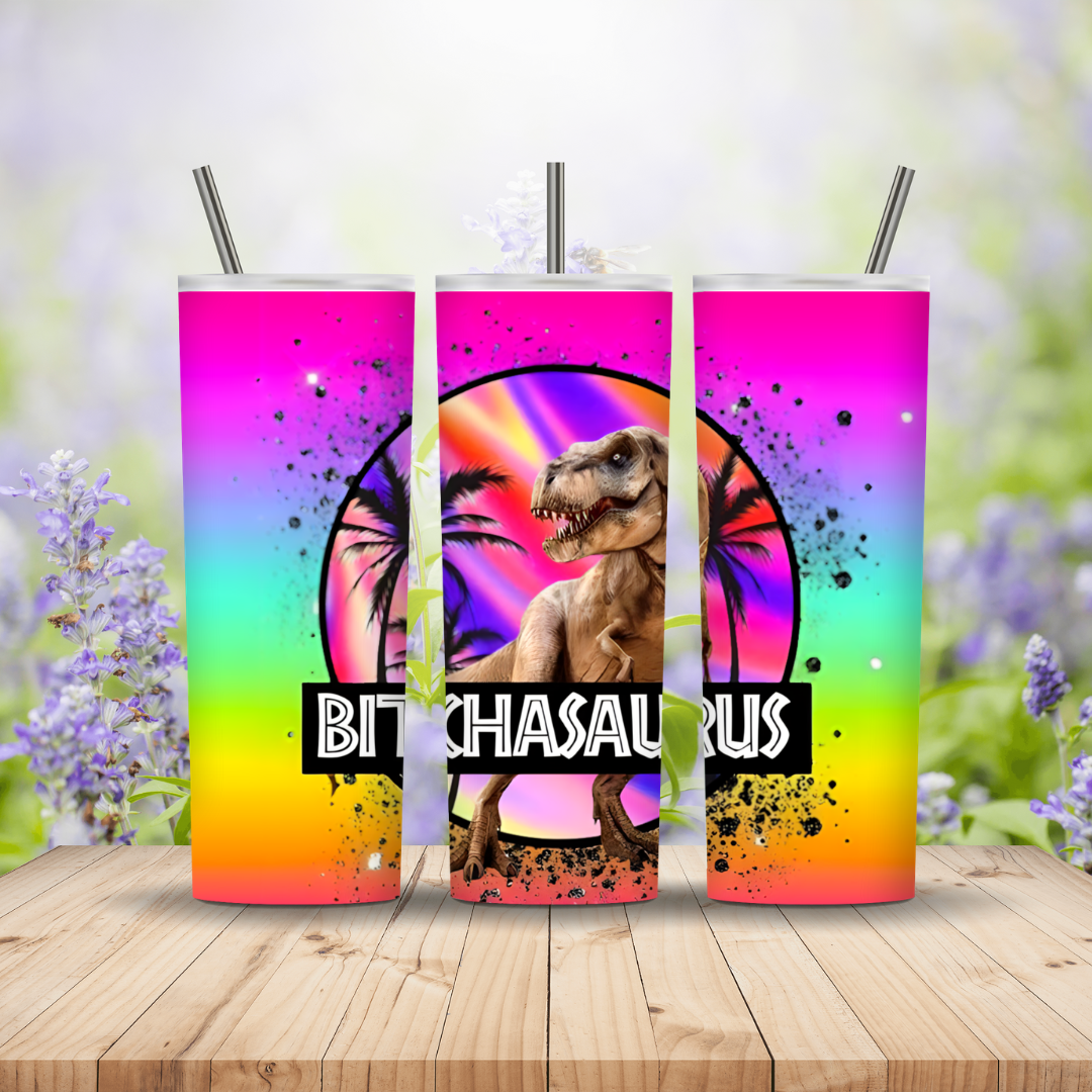 Three colorful tumblers with a dinosaur design and 'BITCHASaurus' text on a wooden surface with a floral background.