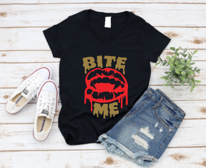 Black t-shirt with bold red vampire lips and dripping "Bite Me" text, styled with white sneakers and ripped denim shorts on a light wooden background.