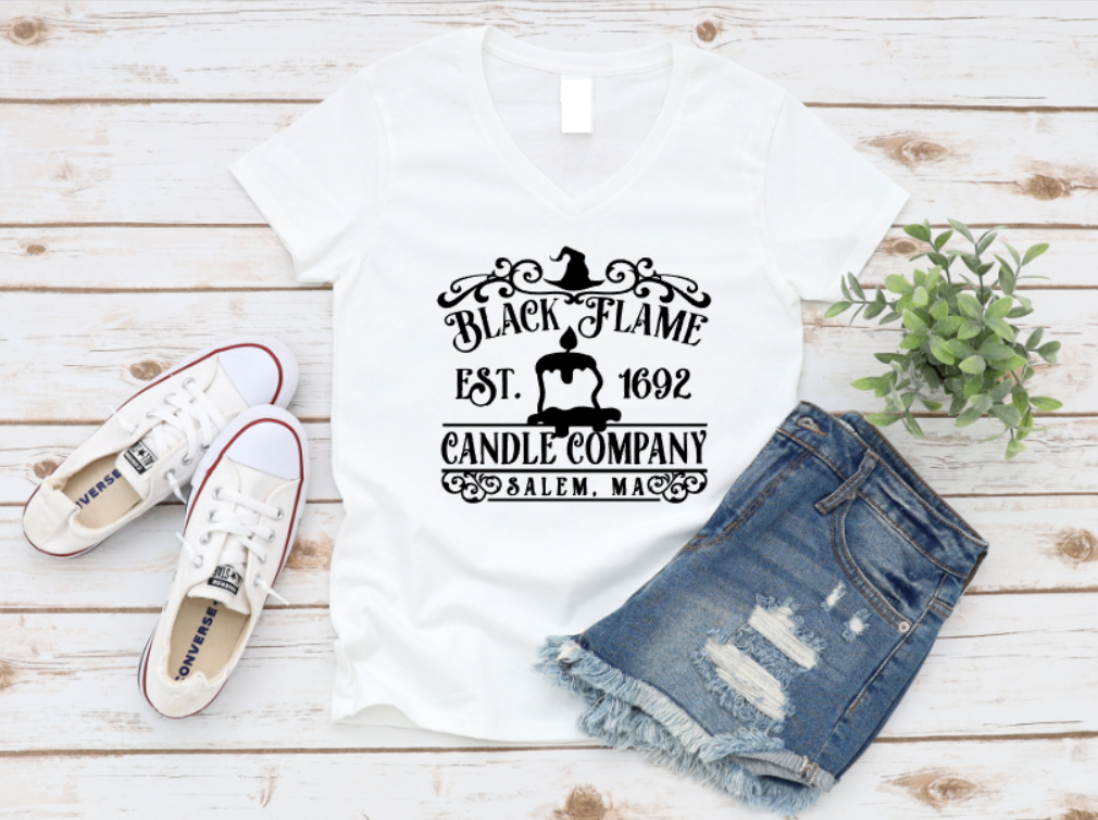 White t-shirt with “Black Flame Candle Company – Salem, MA” graphic, styled with denim shorts and white sneakers on a rustic wooden background.