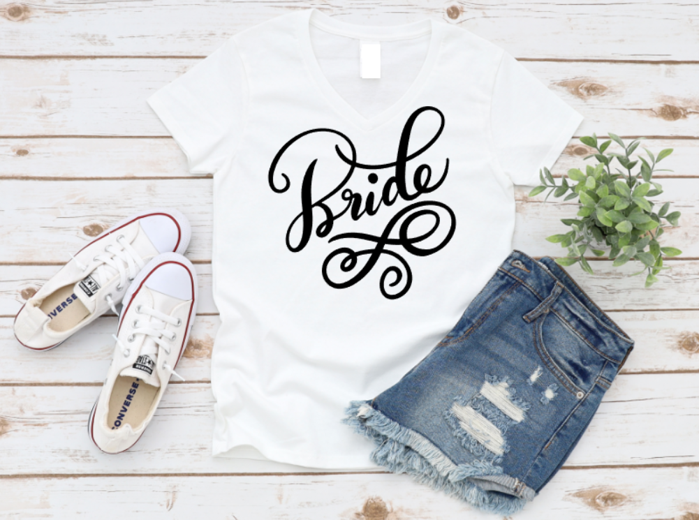 White t-shirt with elegant “Bride” script, styled with ripped denim shorts and white Converse sneakers on a light wood background.