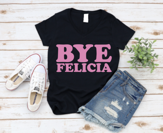 Black t-shirt with bold pink “Bye Felicia” text, styled with denim shorts, sneakers, and a green plant on a wooden background.