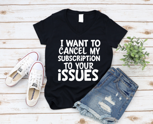 Black t-shirt with the text “I want to cancel my subscription to your issues,” styled with ripped denim shorts, white sneakers, and a green plant on a wooden background.