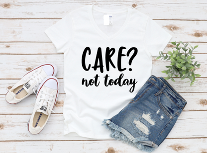 White t-shirt with bold black text "CARE? not today", styled with denim shorts and white sneakers on a wooden background.