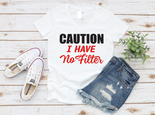White t-shirt with bold white and red text that reads “CAUTION I HAVE No Filter,” styled flat lay with white sneakers and ripped denim shorts on a wooden background.